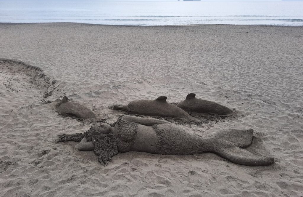 figures of a sandy mermaid and dolphins on the beach