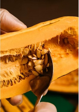 a hand extracting pumpkin seeds with a spoon